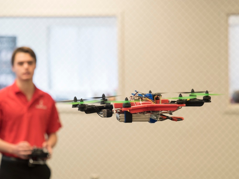 UC student stands in background as a four-rotor drone idles in the air in front of him