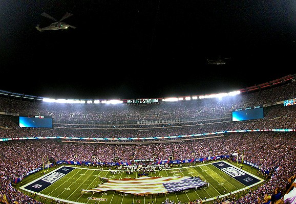 Military carry an American flag onto a football field