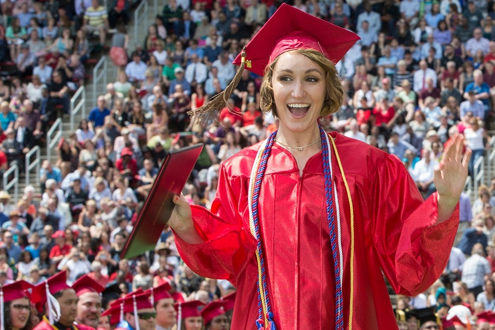  An excited graduate in a red cap and gown holds her degree