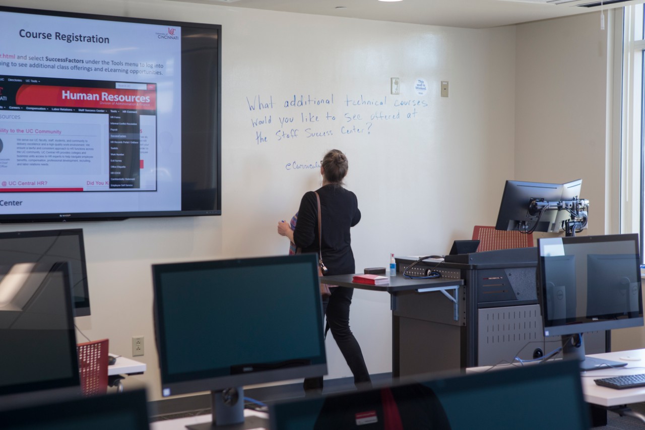 A UC staff member stands inside a room of computers at the Staff Success Center ribbon cutting event.