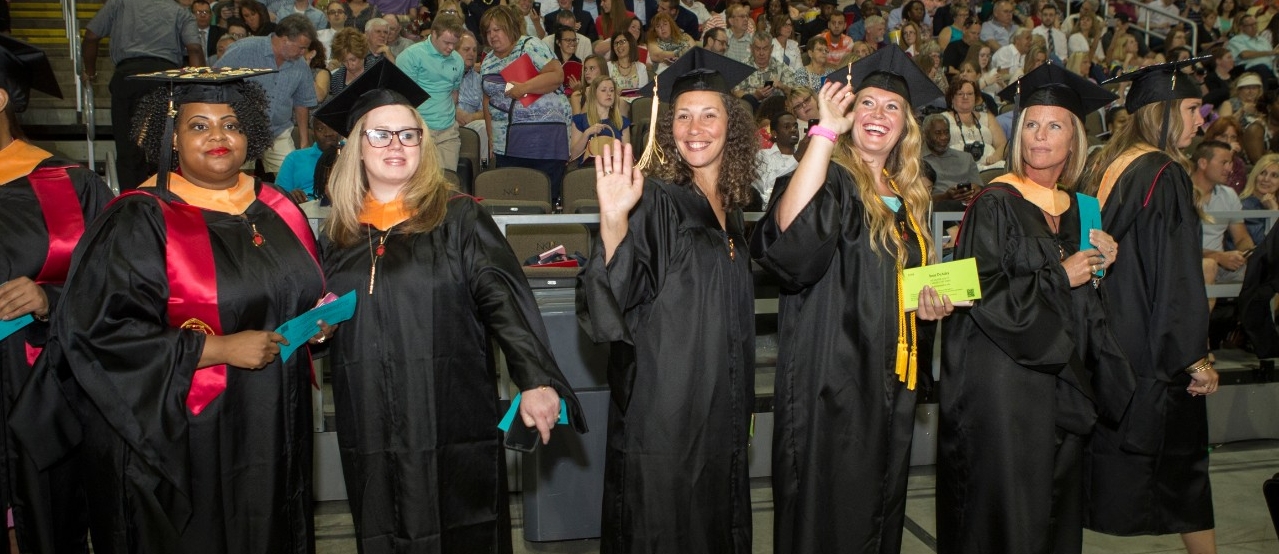 Female graduates in black caps and gowns smile at the audience during UC Commencement