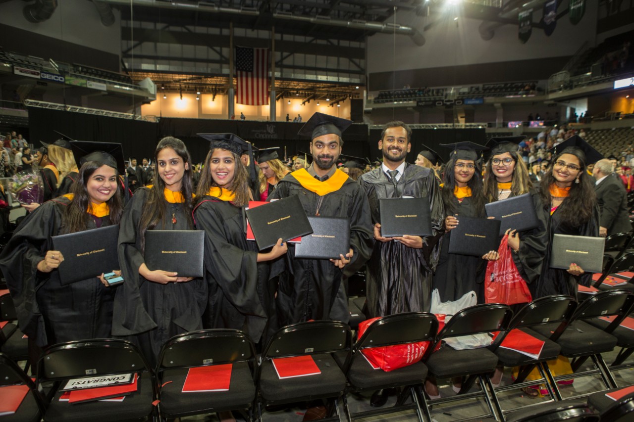 A row of graduates show off their new degrees at UC Commencement.