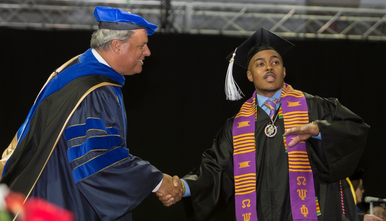 A graduate shakes hands with a faculty member onstage at UC Commencement.