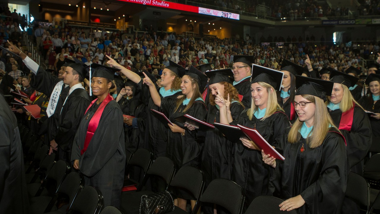 A crowd of graduates in black caps and gowns sing the alma mater at UC Commencement.