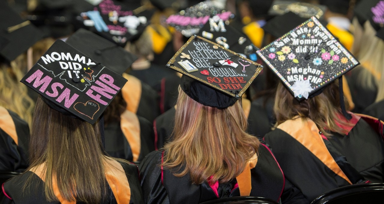 Three female graduates from behind wear graduation caps decorated with the phrases, Mommy did it! and She believed she could, so she did.