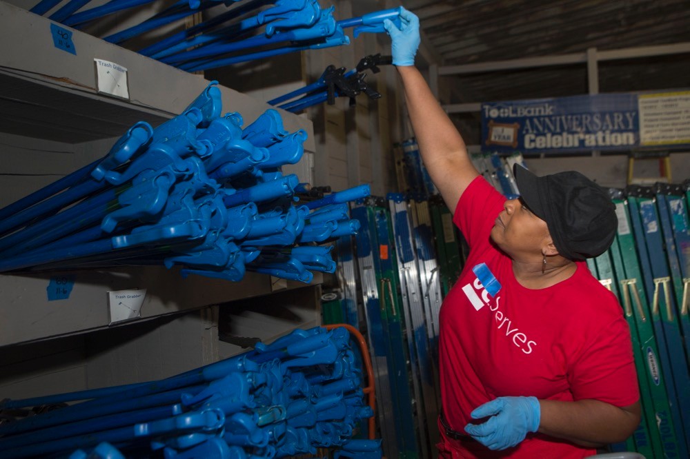 A woman reaches up into a bin of blue long-handled tools.