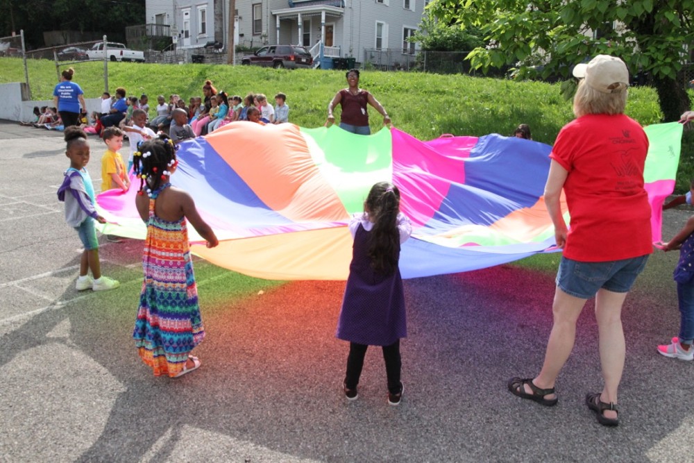 Preschoolers and UC Serves volunteers fluff a giant rainbow parachute.