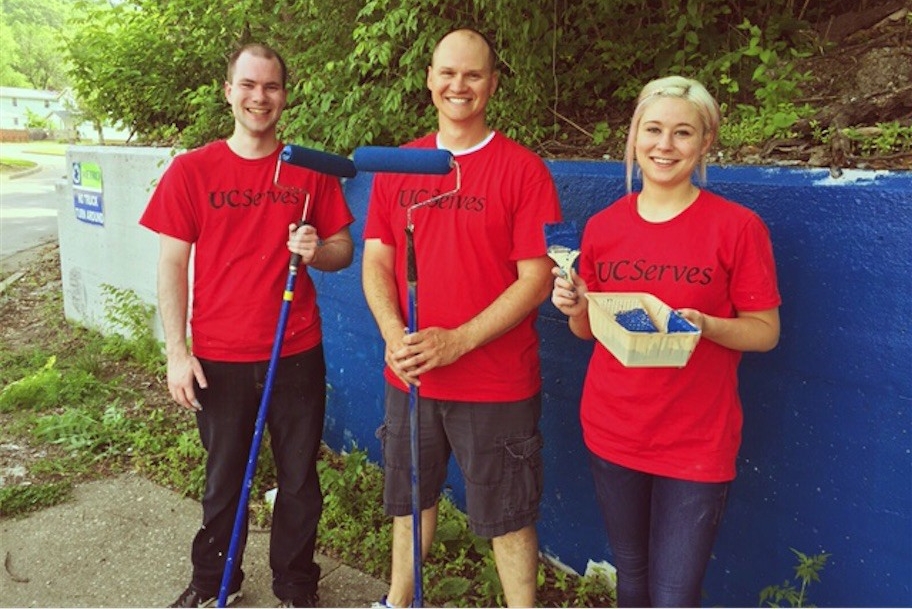 Three UC Serves volunteers stand with paint rollers and brushes.