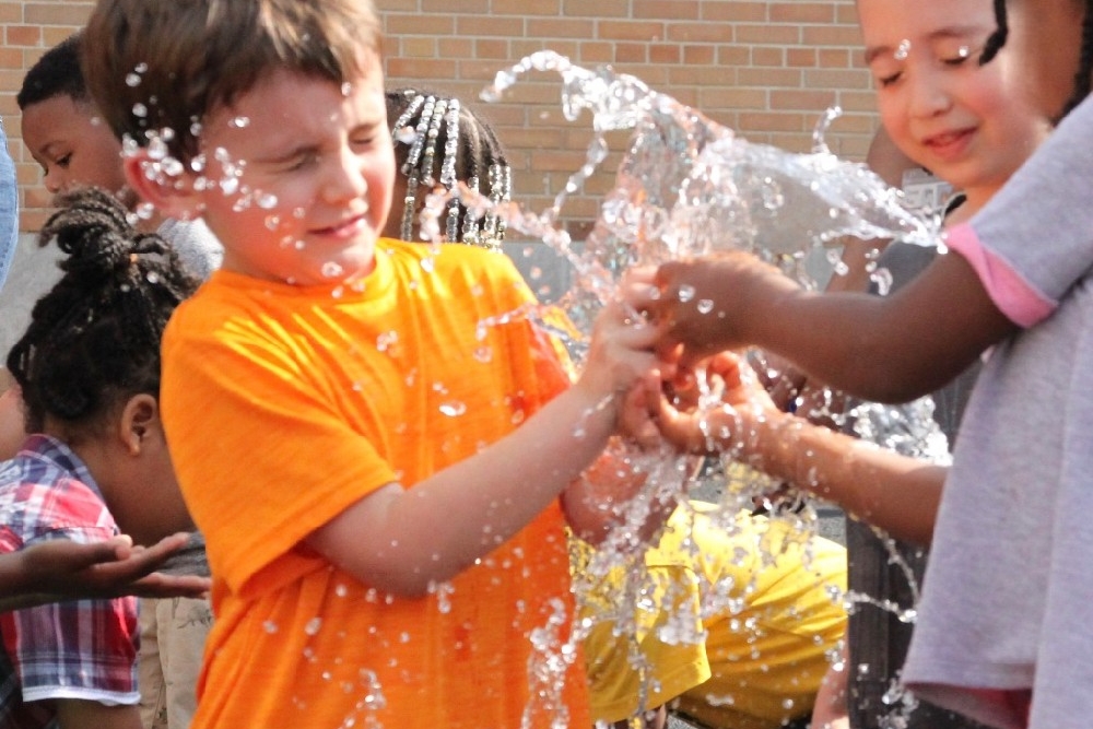 Two children squeeze a water balloon all over their faces at a UC Serves field day.
