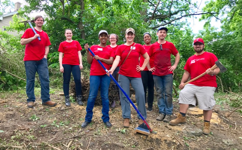 UC Serves volunteers wearing red T-shirts stand with tools and shovels ready to clear an overgrown lot.