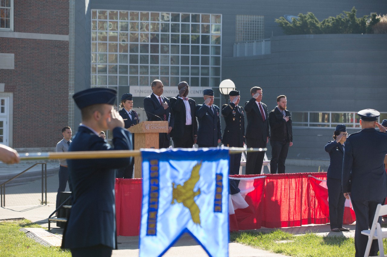 The distinguished speakers stand and salute for the National Anthem. 