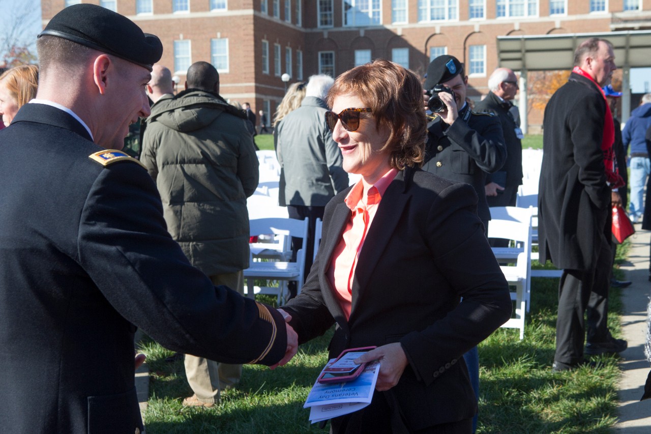 A uniformed male soldier shakes a woman's hand. 