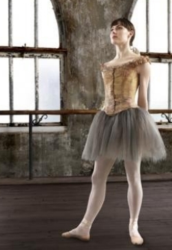 Ballerina star of "Little Dancer" stands in her ballet outfit in a dreary atmosphere of an empty building. 