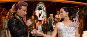A scene between the characters Katniss, dressed in a lovely flowing white gown, and the TV show host Caesar Flickerman.