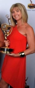 Cara Hannah Sullivan holds her Emmy while wearing an attractive red evening dress.