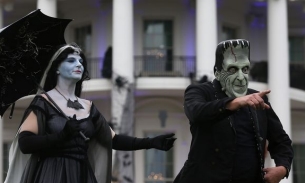 Phil Solomon, dressed as Herman Munster, points at people in the crowd, standing next to "Lily Munster" in front of the White House.