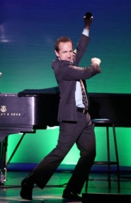 Jason Graae singing and dancing to a piano on stage.