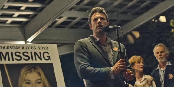 Ben Affleck stands in front of a poster showing his character's missing wife