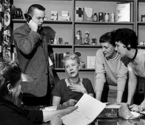 A group of people gather around Ruth Lyons seated at her desk.