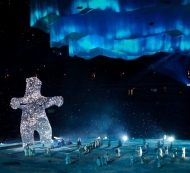 A giant ice bear on the ice rink with skaters around it.