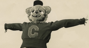 A vintage photograph of a 1950s University of Cincinnati costumed mascot, the Bearcat, leaps mid-air with arms outstretched.