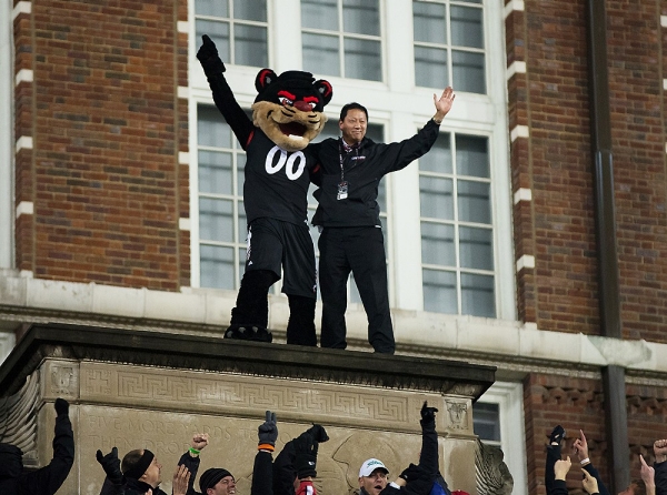 The University of Cincinnati Bearcat mascot and the UC president Santa Ono stand atop the football stadium after being lifted there by the fans.