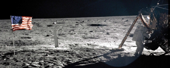 Neil at the moon lander on the moon's surface with the American flag planted in the ground.