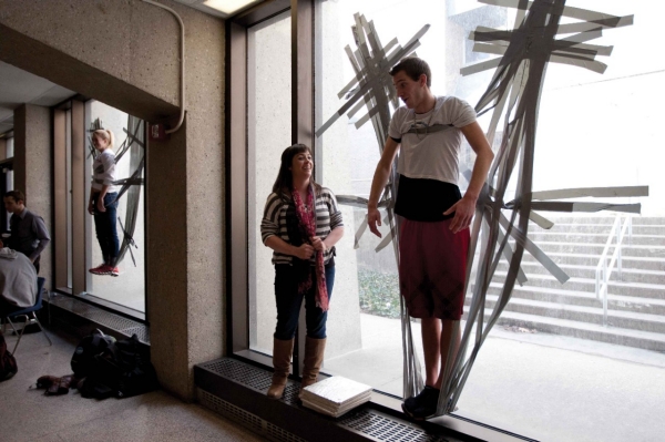 Two students are shown duct-taped to a large plate-glass window.