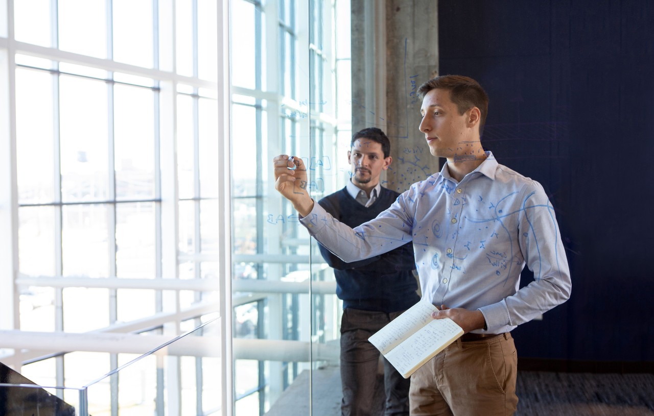 Two people working behind a glass wall and drawing on glass