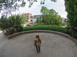 A female student stands with her back to the camera in the center of Echo Point , a circular brick paver structure behind Braustein Hall.
