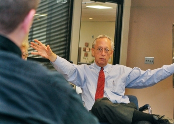 Jim Kautz, seated at his desk in shirt and tie, motions with both arms.