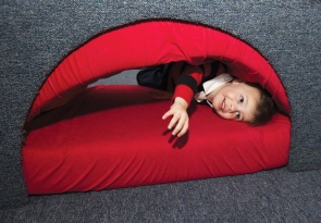 Hobbs Mulligan, a toddler, smiles as he squeezes his way through a red and gray installation piece inside the Contemporary Arts Center.