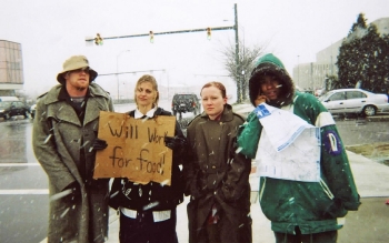 Four members of UC's homelessness experience stand in the snow with a "will work for food sign."