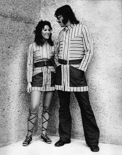 A male and female student from the 1970s stand near Crosley Tower posing in pin-striped threads likely as part of the DAAP Fashion Show.