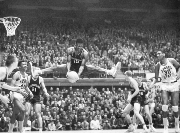 Oscar Robertson rebounds the ball and is suspended in midair with both legs nearly straight out like the splits.