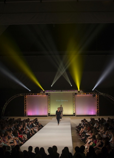 Colorful lights beam up a dark background behind the runway during the UC DAAP fashion show.