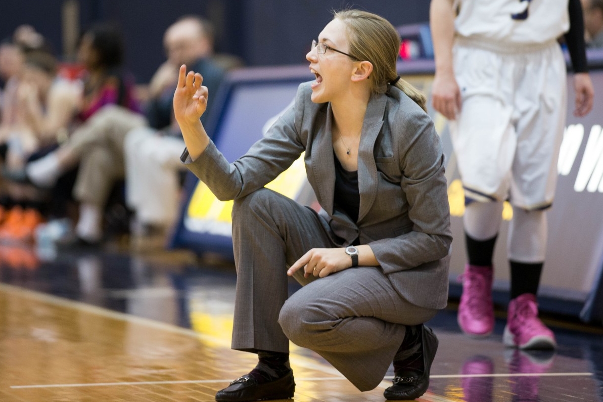 Stephanie Stevens squats along the sidelines signing to her team during a game.