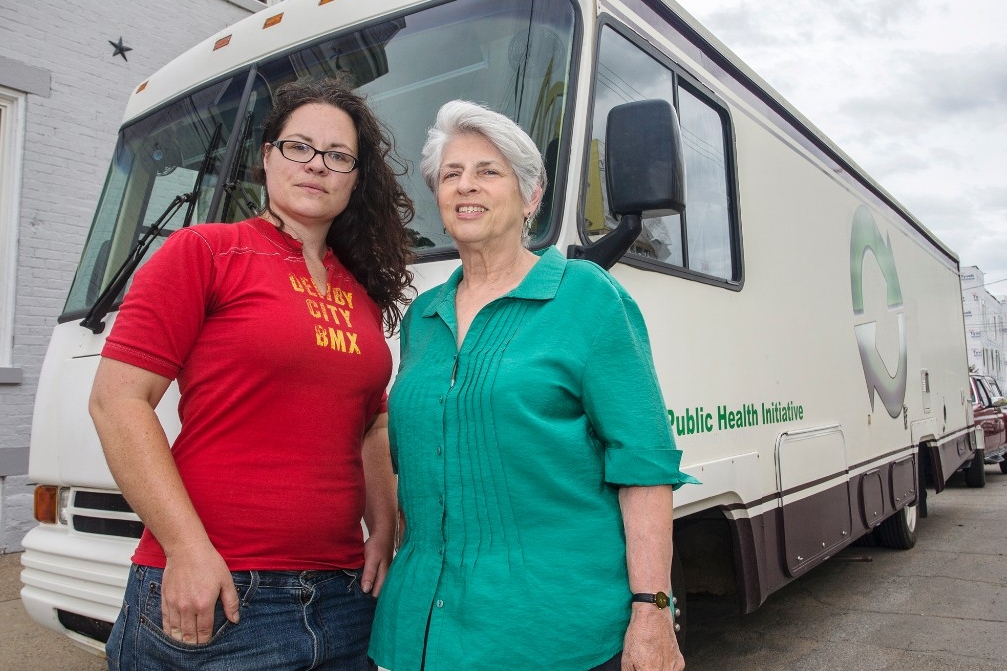 Two women stand before a van they use for a life-saving needle exchange program.