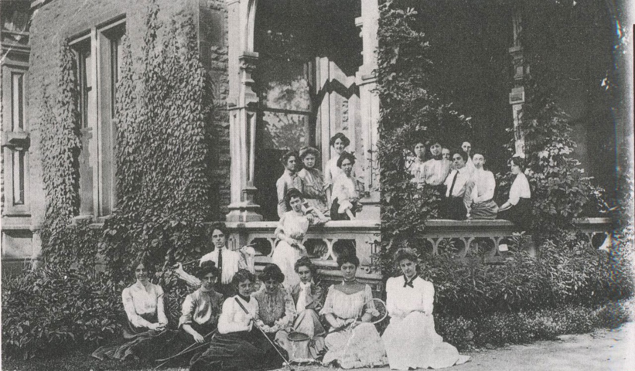 Students sit and stand outside a home in early 1900s