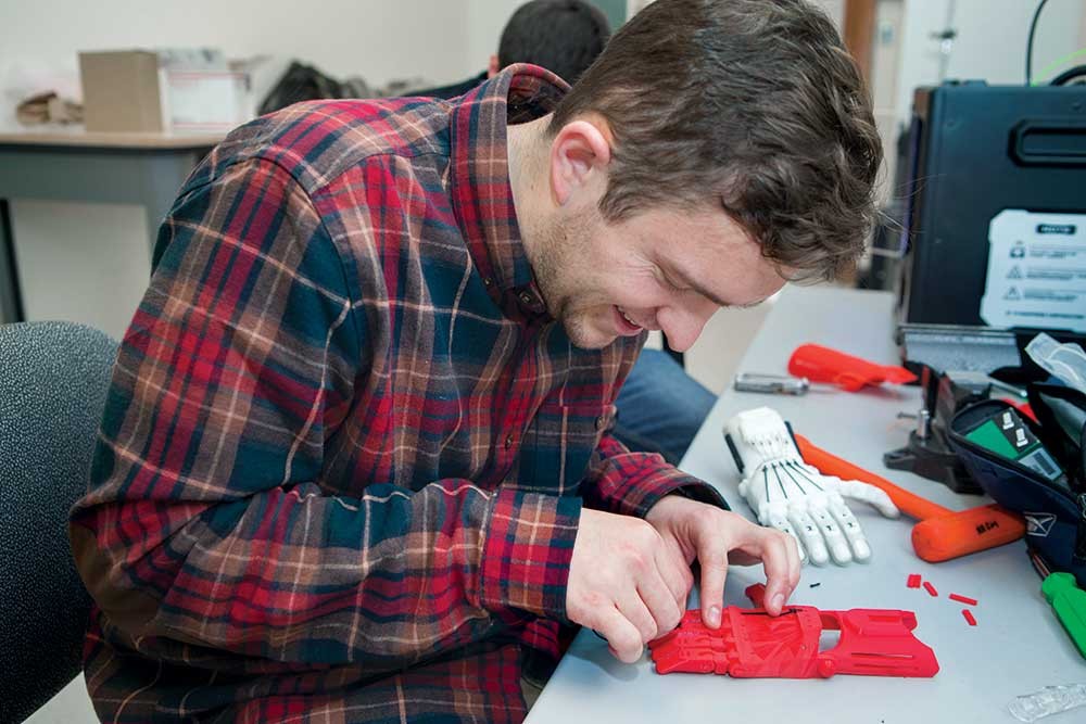 Jacob Knorr assembles prosthetic hands at a workbench.