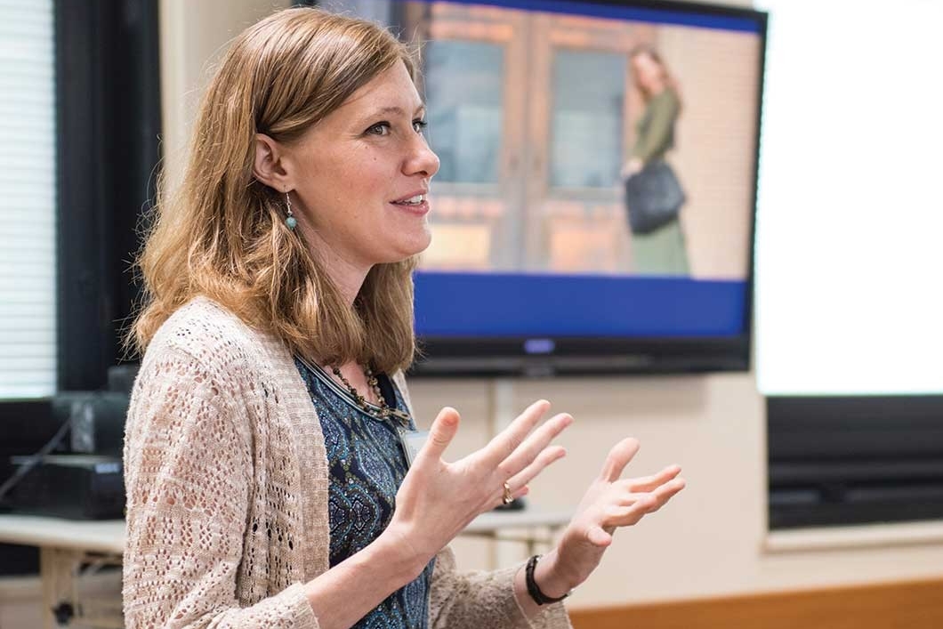 Bethany Yeiser gestures with her hands as stands and speaks in front of a UC classroom.