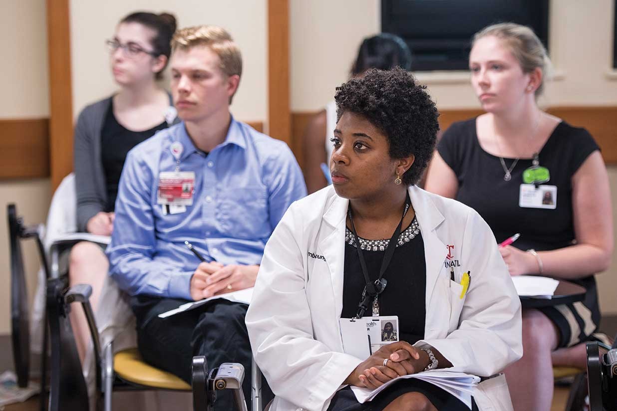 Several UC Medical residents sit in desks while listening to Bethany Yeiser speak.