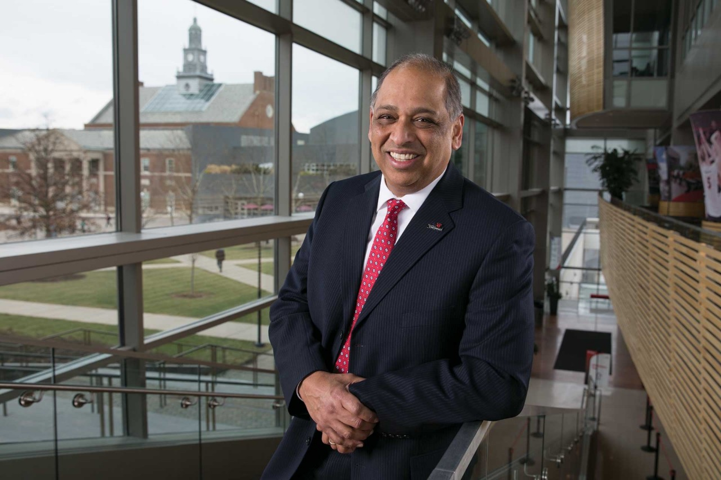 Portrait of President Pinto leaning on the staircase of University Pavilion with campus in the background.