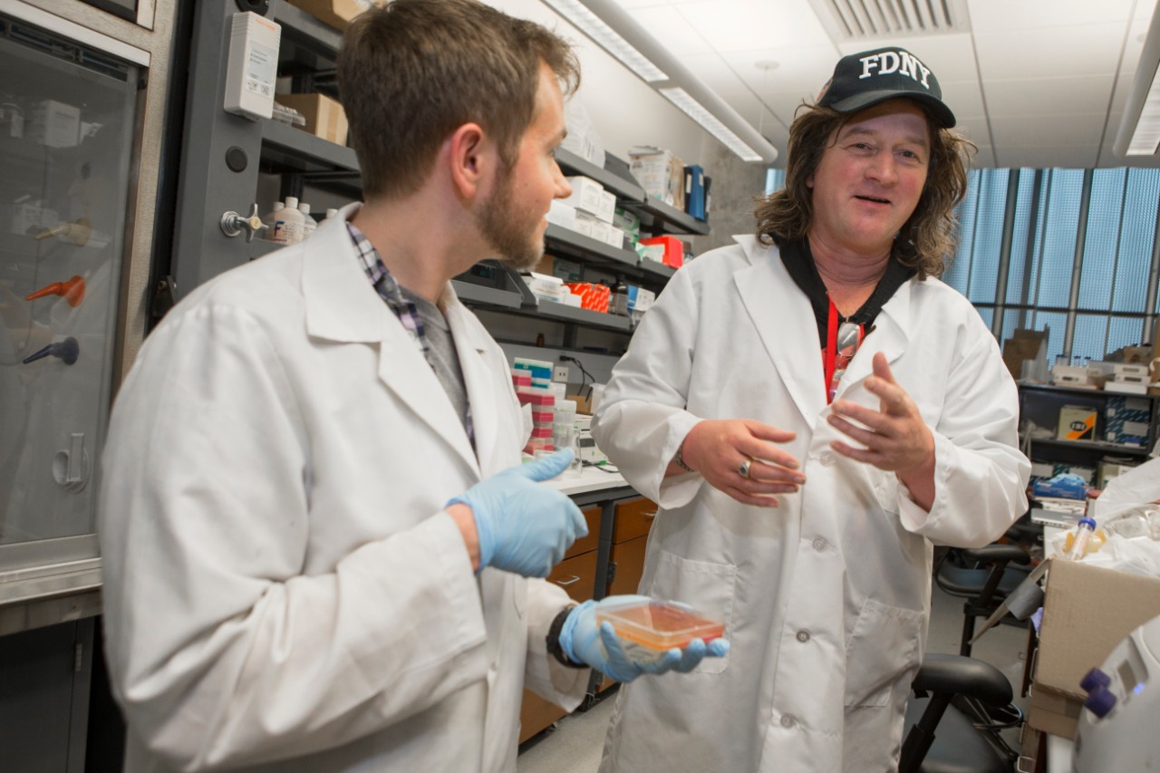 Former doctoral student Cameron McDaniel interacts with researcher Daniel Hassett in the lab.