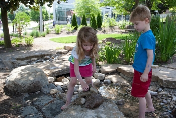 Twins Lily Hope and Abbott Hoffman-Suder stack rocks in a creek bed at UC's PlayScape.