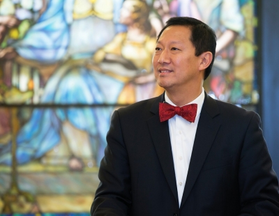 UC President Santa Ono looks reflective next to a stained glass window.